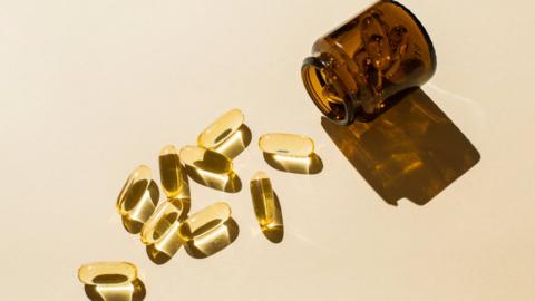 A bottle of supplements with some capsules which are laid out on a surface