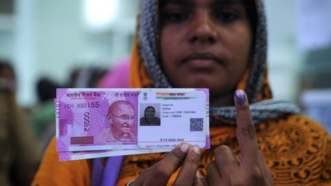 A Indian woman poses with new 2000 rupee notes, her Aadhaar ID card and a finger inked with indelible ink after exchanging withdrawn 500 and 1000 rupee banknotes at a bank in Chennai on November 17, 2016