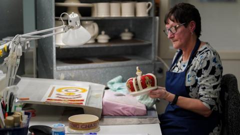 A pottery decorator adds details to a crown, during the production of hand-decorated pieces from the forthcoming King Charles III Coronation collection, at the Emma Bridgewater Pottery Factory in Stoke on Trent.