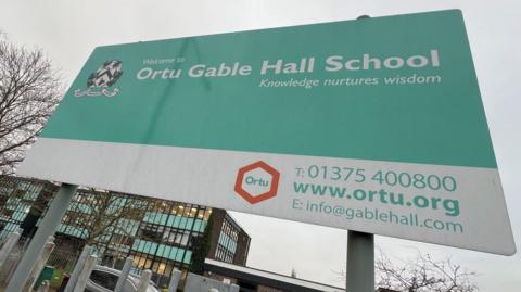 A green and white sign at the entrance to Mossbourne Fobbing, advertising its previous Gable Hall School name. A large school building is behind the sign.