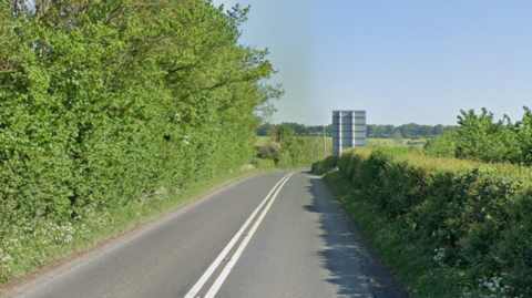 Google Maps street view of the A338 Tidworth Road in Wiltshire. The road is approaching a bend to the right. There are bushes and shrubs either side of the road.
