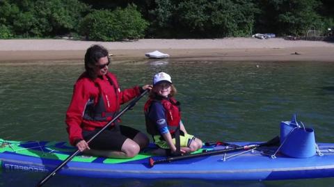 Ella and her mum on a paddleboard on a river.