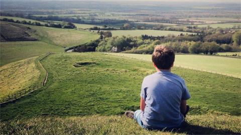 Boy sitting on hill looking at countryside