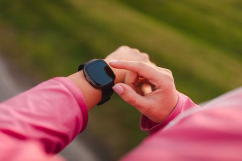 A smartwatch is seen on the hands of a person wearing a pink top