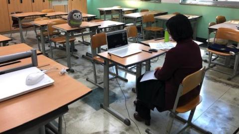 A teacher sits in an empty classroom