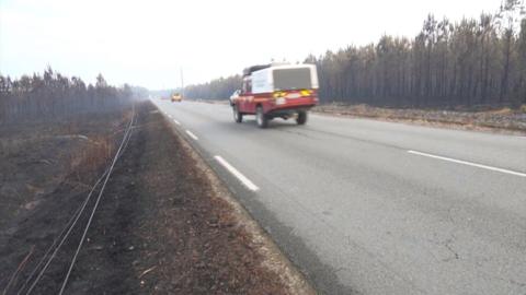 A firetruck travels down a road with burnt vegetation on either side