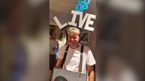 Dan Ellis dressed in his Co-Op Live Halloween outfit, featuring a cardboard box held up by suspenders and a large headpiece bearing the name of the arena. 