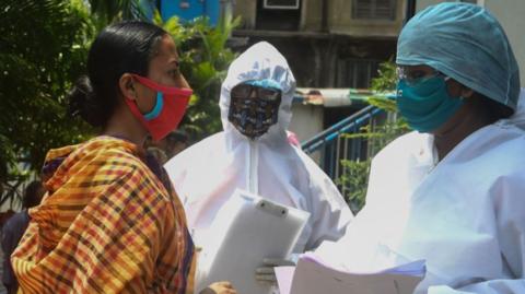 Municipal workers in hazmat suits talk to people waiting for a checkup at a municipal health camp during a government-imposed nationwide lockdown as a preventive measure against the COVID-19 coronavirus, in Kolkata on April 29, 2020.