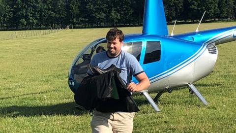 Adam holding bag as he walks from a helicopter