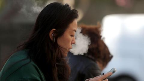 A pedestrian smokes an e-cigarette in San Francisco, 2019