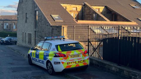 A police car is parked on the pavement alongside an iron fence.