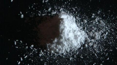 A close-up of a small mound of white powder on a black counter. The right-hand side is illuminated while the left is in shadow.