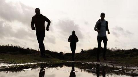 The silhouette of three men running through the countryside.