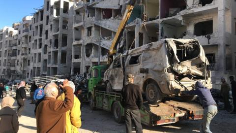 People remove a destroyed vehicle from the scene of an explosion in Idlib city, Syria (8 January 2018)