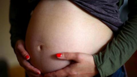 Pregnant woman wearing red nail varnish holding stomach