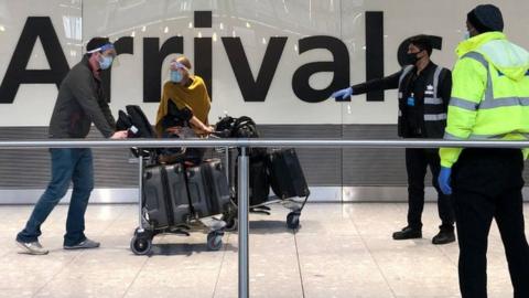 Passengers are escorted through the arrivals area of Heathrow Terminal Five, towards coaches destined for quarantine hotels