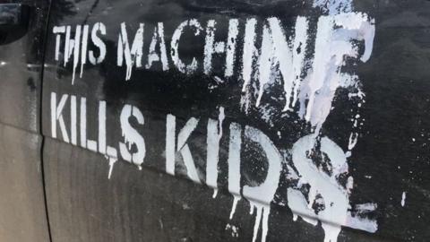 A car spray painted with the slogan 'This machine kills kids' in white paint