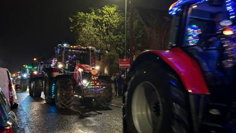 Tractors decorated in flashing lights driving along a road in the dark