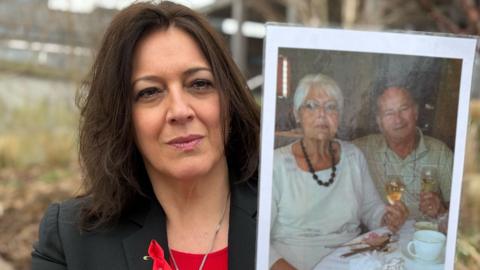 A woman sat down holding a photo of a man and a woman.