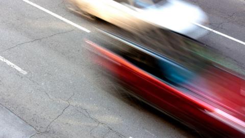 A blurred photo of a white car and red car speeding on a road