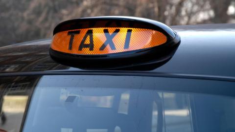 The roof of a black cab has a bright orange illuminated sign saying Taxi