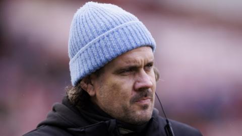 Gloucester-Hartpury Women's Rugby club head coach Dan Murphy looks on, wearing a light blue woolly hat