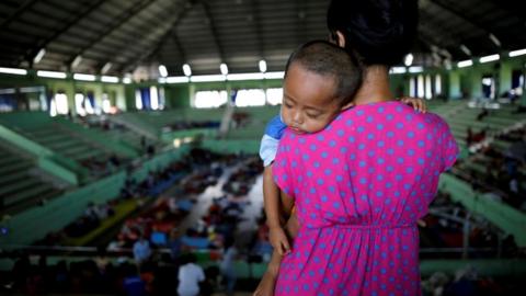 A boy is seen asleep on his mothers shoulder in a evacuee shelter inside of a sports hall