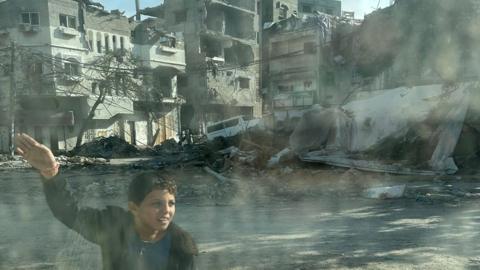 A boy stands in front of destroyed buildings in the Gaza Strip