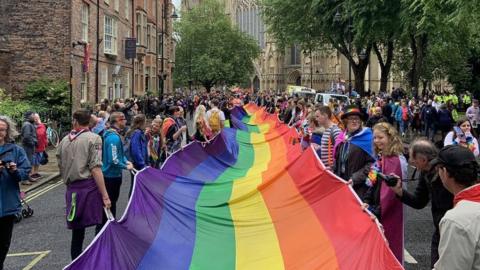 People holding a very long flag as they parade through a York street