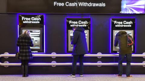 Three people standing at cash machines