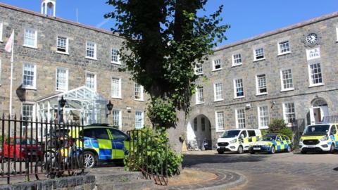 A view of Guernsey Police station. Showing the brick building and police cars parked outside.