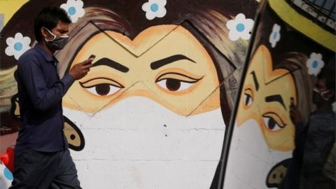 A man walks past a graffiti of a girl wearing a protective mask amidst the spread of the coronavirus disease (COVID-19) on a street in Navi Mumbai, India January 21, 2021.