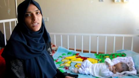 Five-month-old Abdulaziz al-Hourani lies in his bed at al-Ahli hospital in northern Gaza, accompanied by his mother, who is dressed in a black abaya