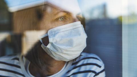 Stock image of woman wearing a mask at a window