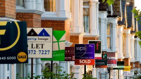 Row of houses with For Sale, Sold and To Let signs in front of them 