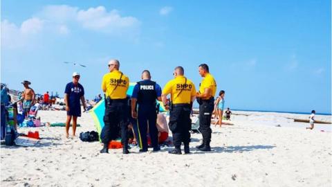 Police on beach surrounding injured woman