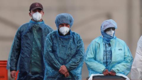 Passengers draped in medical blue PPE disembark cruise ship