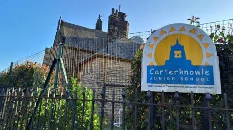 An older brick-built school building has railings and a blue and yellow sign saying Carterknowle Junior School