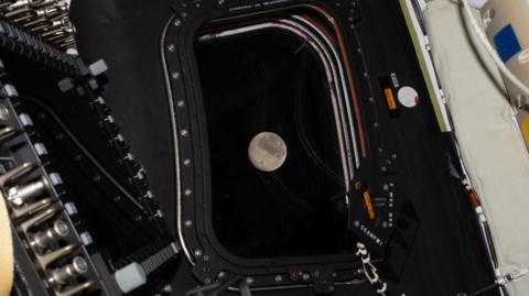 The Moon is pictured through a window of a spacecraft.