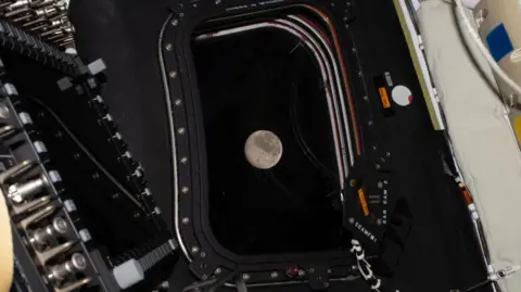 The Moon is pictured through a window of a spacecraft.