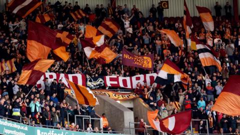 Dozens of orange and amber flags waved by a crowd of supporters at a football game