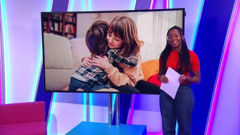 emma-louise smiling next to a tv with an image of two kids hugging