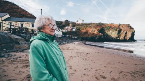 Menyw'n crwydro'r traeth gwag yn Llangrannog