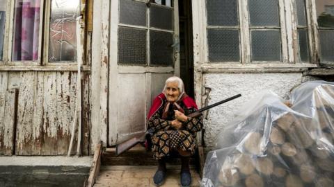 Old woman stands in the entrance of her home with a rifle during the shelling of Stepanakert city