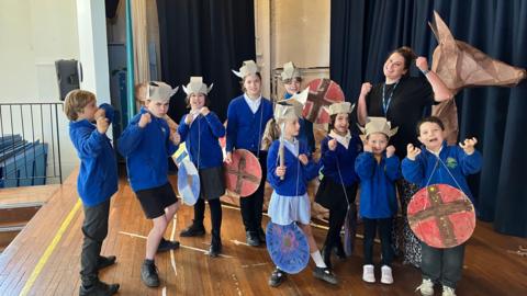 A group of pupils pretend to be vikings in front of a viking longboat
