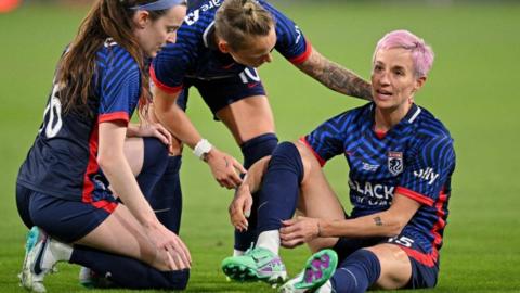 OL Reign forward Megan Rapinoe is checked on by team-mates Rose Lavelle and Jessica Fishlock after suffering an injury in ger farewell game
