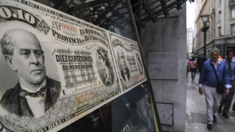People walk past a bank's branch decorated with images of old Argentine peso bills, in Buenos Aires, on September 26, 2018.