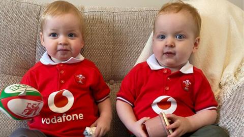 Ella and Isaac on a settee wearing wales rugby jerseys