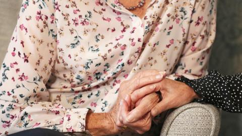 Care home resident holding hands with her daughter