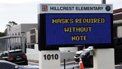 Parents drop their kids off at Hillcrest Elementary school in Orlando with a sign at the entrance advising 'masks required without note'